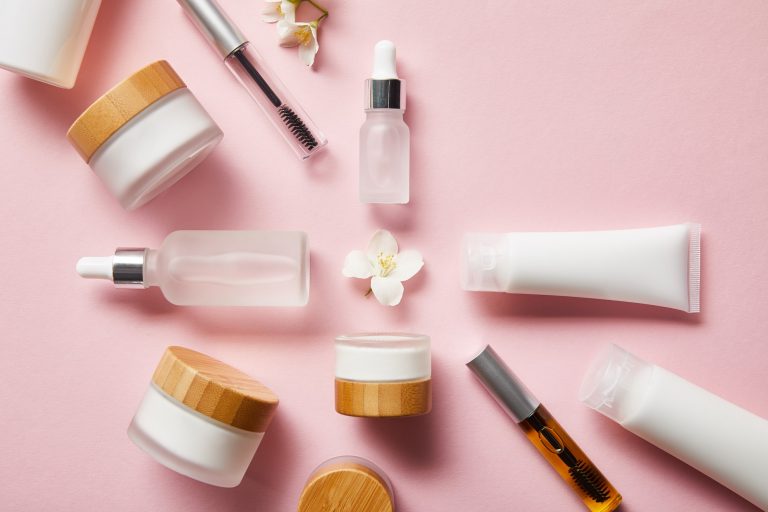 top view of jars, cream tubes with hand cream, cosmetic glass bottles, mascara bottles and jasmine